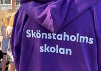 Ryggtavlan på en personal som har en lila tröja med vit text som säger Skönstaholmsskolan