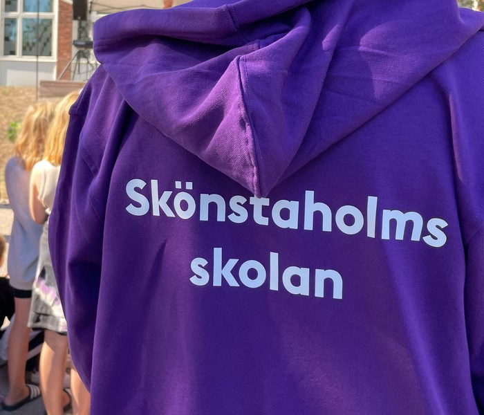 Ryggtavlan på en personal som har en lila tröja med vit text som säger Skönstaholmsskolan