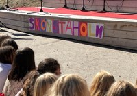 Barnryggar som sitter framför en scen med en skylt med texten Skönstaholm
