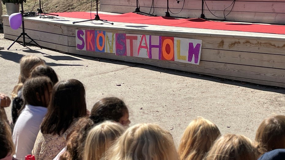 Barnryggar som sitter framför en scen med en skylt med texten Skönstaholm