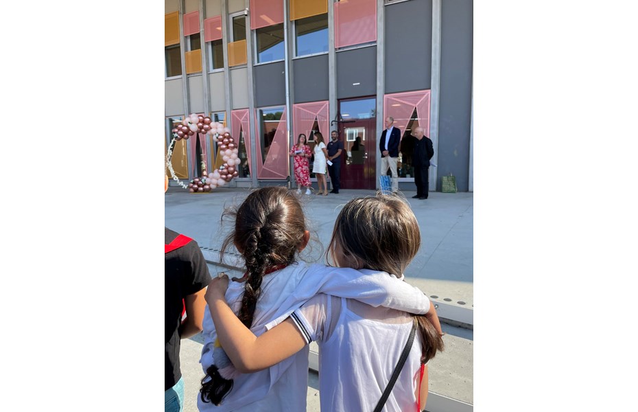 Två skolbarn i förgrunden, när skolans och stadens representanter invigningstalar framför den nya skolbyggnaden.